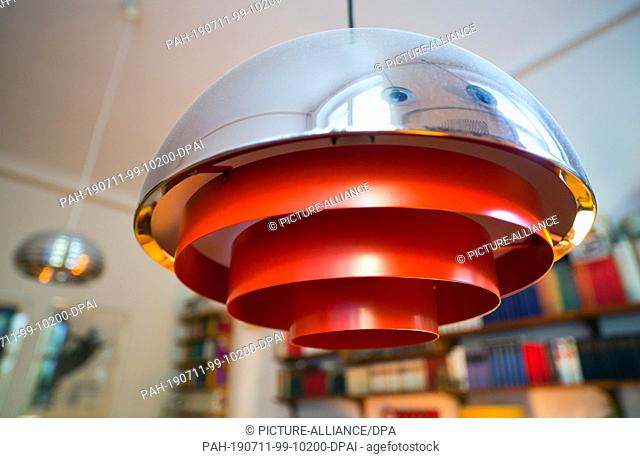 02 July 2019, Germany (German), Berlin: A dining table lamp by Jo Hammerborg with the name ""Milieu"" hangs in an apartment