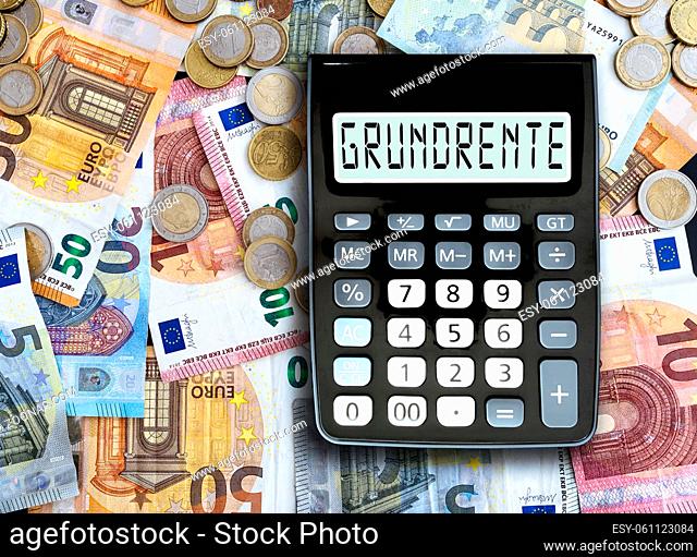 top view of German word GRUNDRENTE, basic pension, written on display of pocket calculator against cash money on table