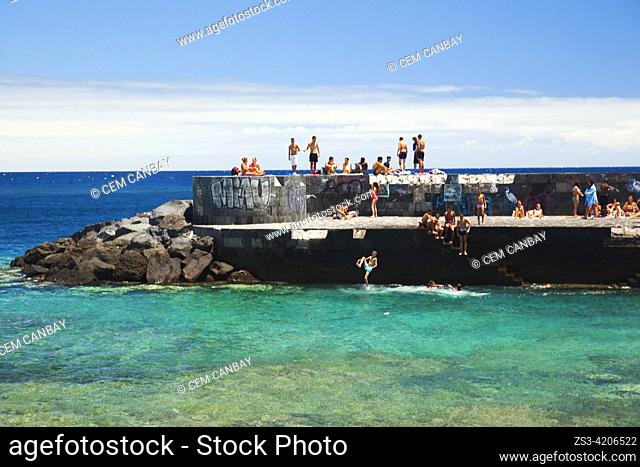 Young people sunbathing and some of them jumping into the water from the pier, Santa Cruz, Tenerife, Canary Islands, Spain, Europe