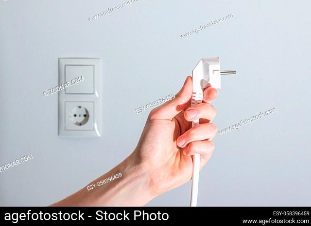 White plug with cable in males hand, ready to connect. Energy concept