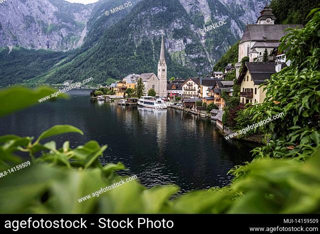famous lake side view of hallstatt village with alps behind, foliage leaves framed. austria