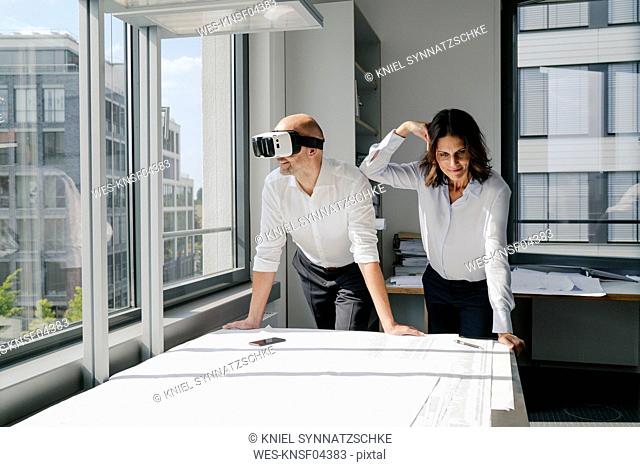 Two architects working on blueprints, man using VR glasses
