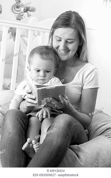 Black and white portrait of young mother sitting with baby in beanbag and reading book