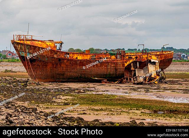 A rusty shipwreck in the mud of the Walney Channel, seen from the road to Roa Island, Cumbria, England, UK