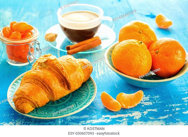 cup of coffee, croissant, and mandarines on blue background