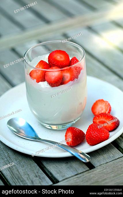 Glass with yogurt and strawberries on wooden board
