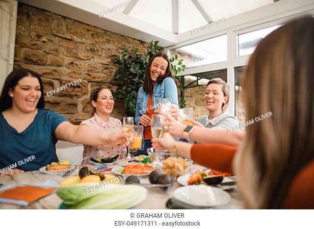 Small group of female friends preparing a healthy lunch inside of a conservatory on a weekend away. They are making a celebratory