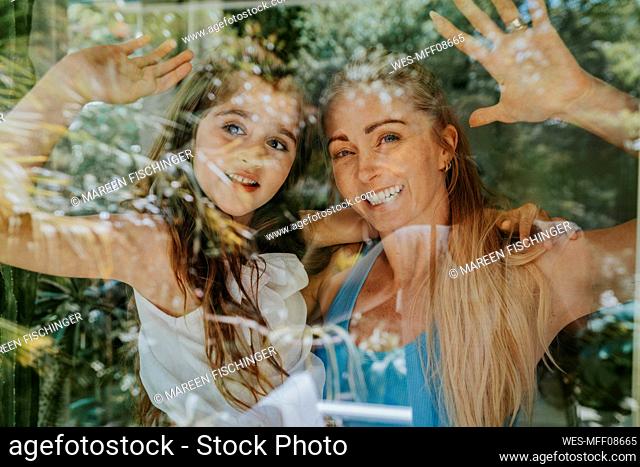 Smiling mother and daughter waving through window of house