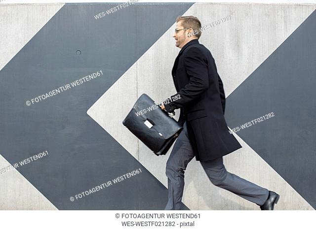 Businessman with briefcase running along wall