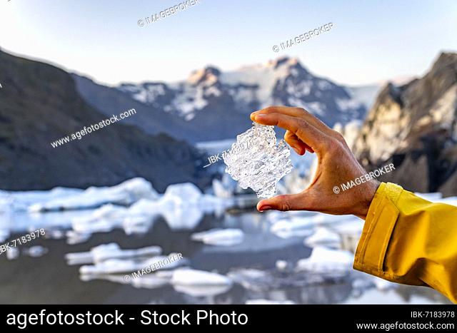 Hand holding glacial ice, Svínafellsjökull glacier, Hvannadalshnúkur mountain behind, Vatnajökull National Park, Skaftafell, South Iceland, Iceland, Europe