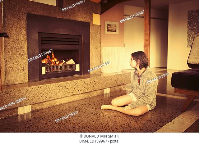 Mixed race girl relaxing by fireplace in living room