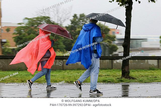 People in rain clothes and with umbrellas walk through the Tiergarten under pouring rain and temperatures of 16 degreees Celsius in Berlin, Germany