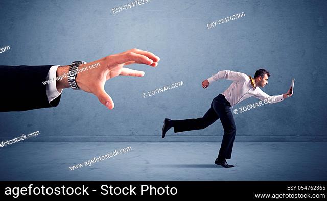 Young miniature businessman running from a big hand with blueish background