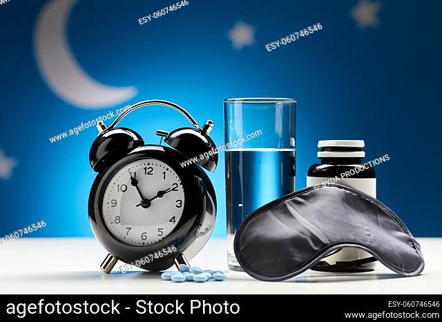 alarm clock, glass of water and sleeping pills