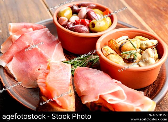 Tapas of salmon, mussels, jamon and olives on ceramic plate