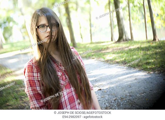 A casual portrait of a 26 year old woman with long brown hair and big glasses, on a country road