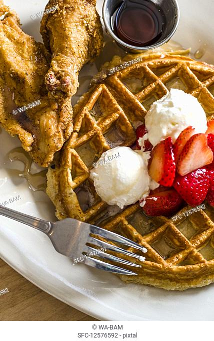 Belgian waffle topped with butter, strawberries and syrup with fried chicken