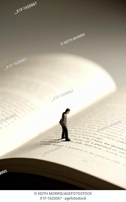 a small figure of a man walking on an open book - conceptual image for literacy and reading