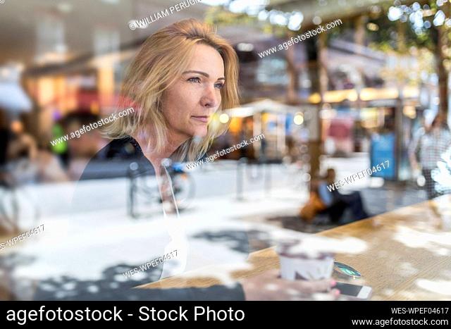 Thoughtful woman looking through window while sitting in cafe