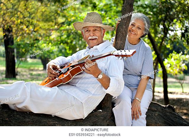 Senior man playing guitar while enjoying at park with mature woman