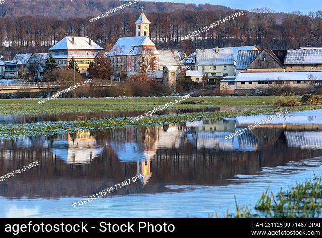 25 November 2023, Baden-Württemberg, Riedlingen: The snow-covered church of St. Gallus in Riedlingen Zell is reflected in a flooded meadow