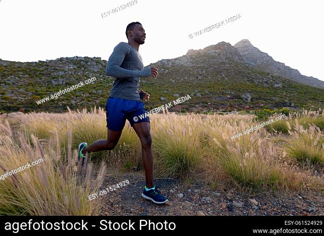 Fit african american man in sportswear running through tall grass