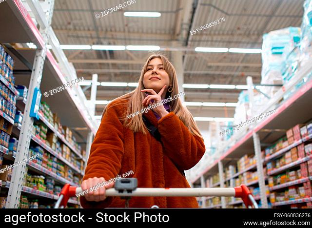 Young woman with grocery cart and shelves with groceries in a store