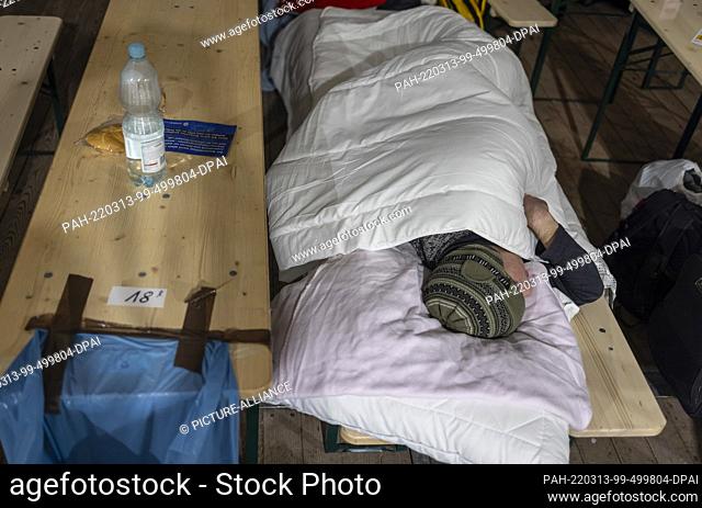 13 March 2022, Berlin: A man sleeps on beer benches in a tent for refugees from Ukraine in front of the main train station