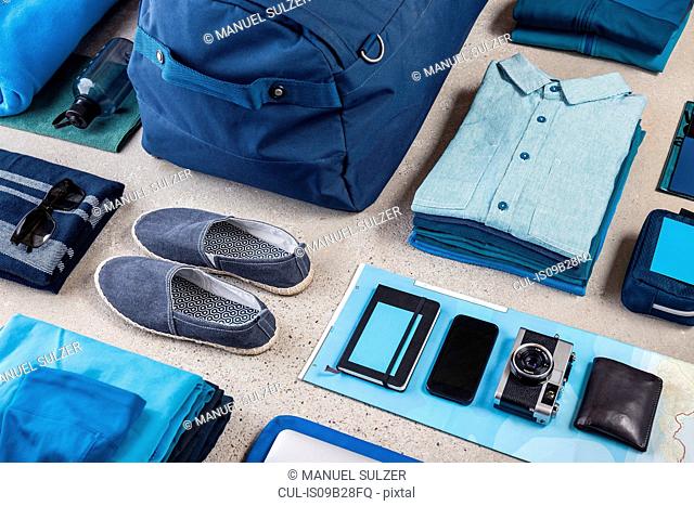 Overhead view of travel packing with blue shirt, retro camera, training shoes, smartphone and notebook