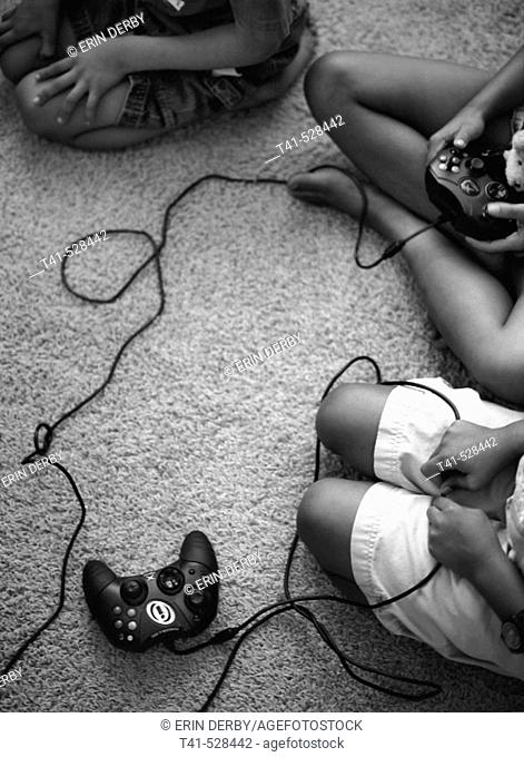 Brothers and sisters sit on the rug playing video games. Some anxiously await the turn at the remote. All watch the TV