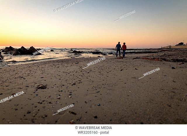 Senior couple walking on beach during sunset