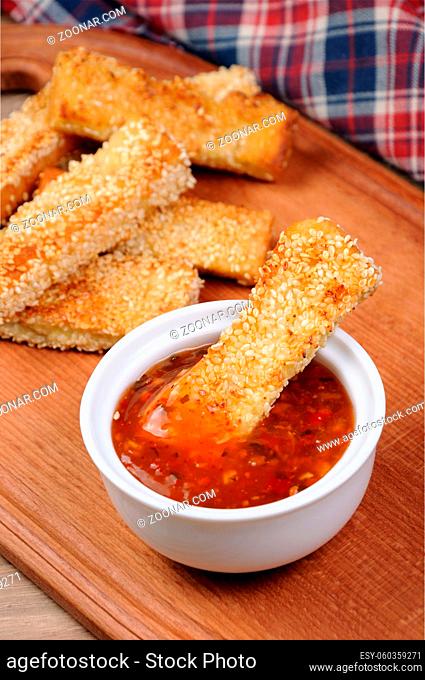 Slice of toast roasted in breaded with cheese and sesame slipped in a sauce on a wooden board