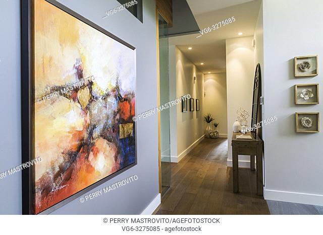 Framed abstract painting on grey wall of hallway with hickory wood floorboards inside a luxurious contemporary bungalow style home