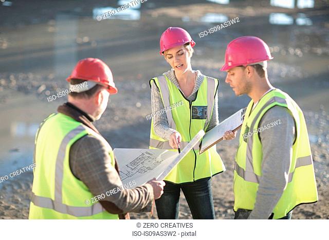 Architect and builders pointing to blueprint on construction site