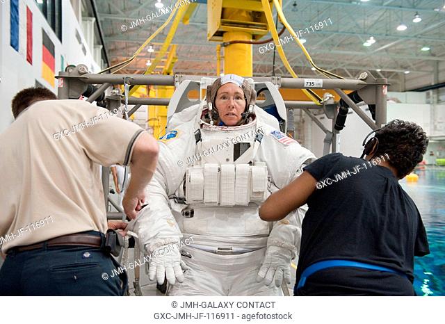 NASA astronaut Sandy Magnus, STS-135 mission specialist, gets help donning a training version of her Extravehicular Mobility Unit (EMU) spacesuit in preparation...