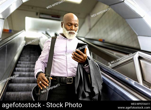 Senior commuter with laptop bag using smart phone on escalator
