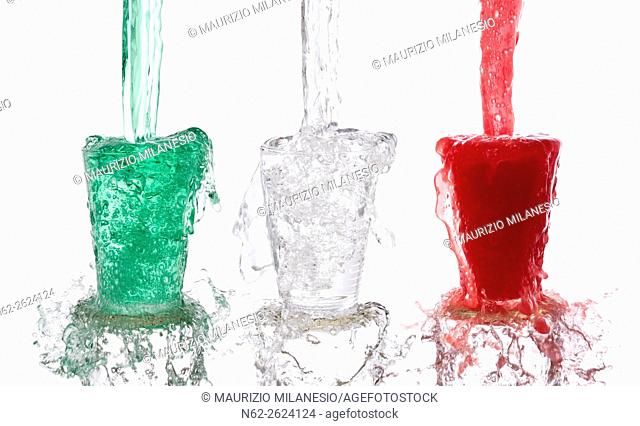 Tricolor drinks poured vigorously into three overflowing glasses on white background