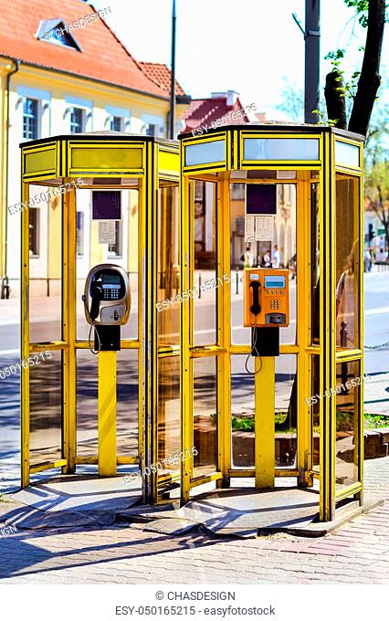 Yellow glass telephone booths with payphones are located on a pedestrian street. Obsolete means of telephone communication in free access