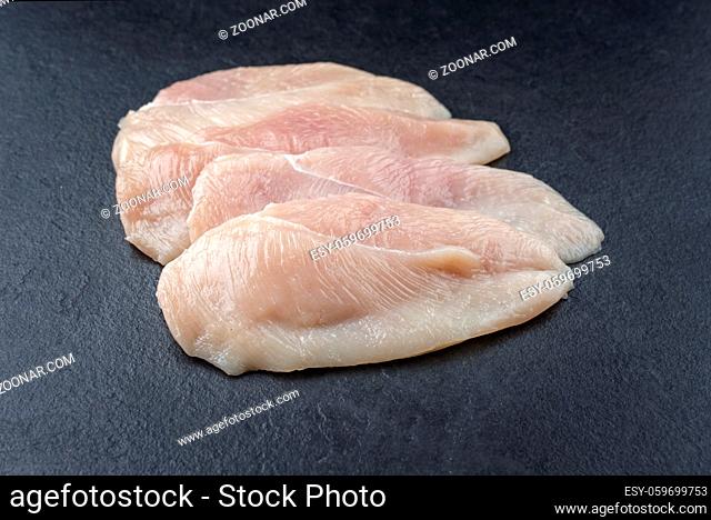 Raw traditional chicken escalope filets offered as close-up on a black board with copy space