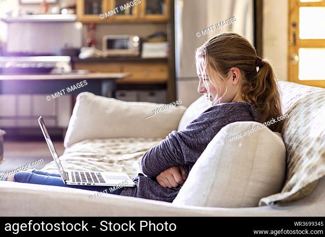 Teenage girl looking at laptop on sofa