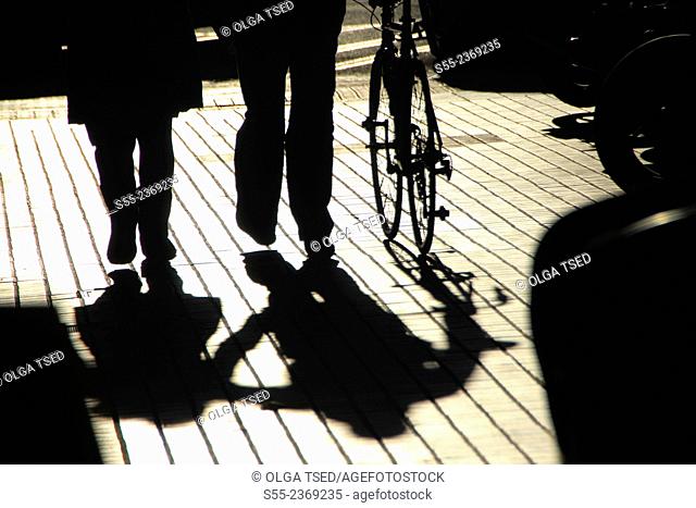 Pedestrians strolling with a bicycle and their shadows. Barcelona, Catalonia, Spain