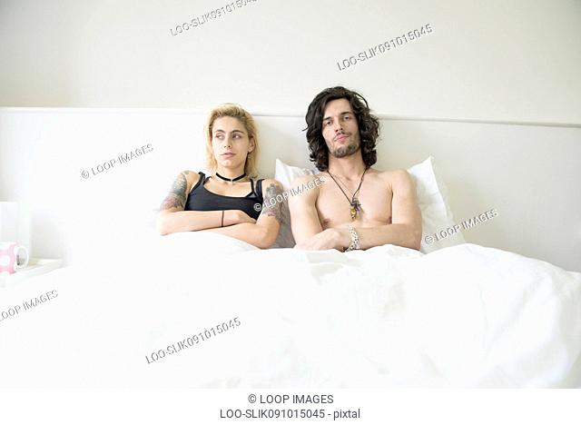 A cool young tattooed couple lying in a double bed after an arguement