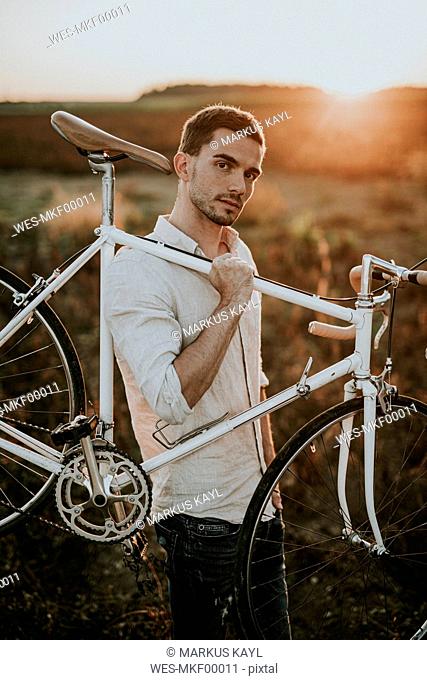 Pensive young man carrying a racing cycle in the sunshine