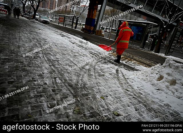 11 December 2023, China, Peking: An employee of the Beijing city cleaning service shovels snow. It snowed heavily in Beijing on Monday night