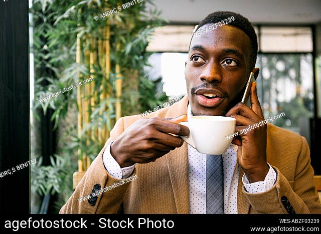 Young businessman drinking a cup of coffee and talking on the phone in a cafe
