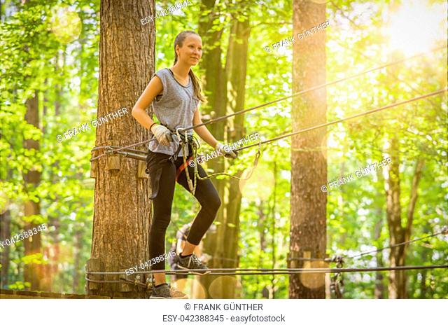 young, blond girl climbs in summer in climbing forest / high ropes course