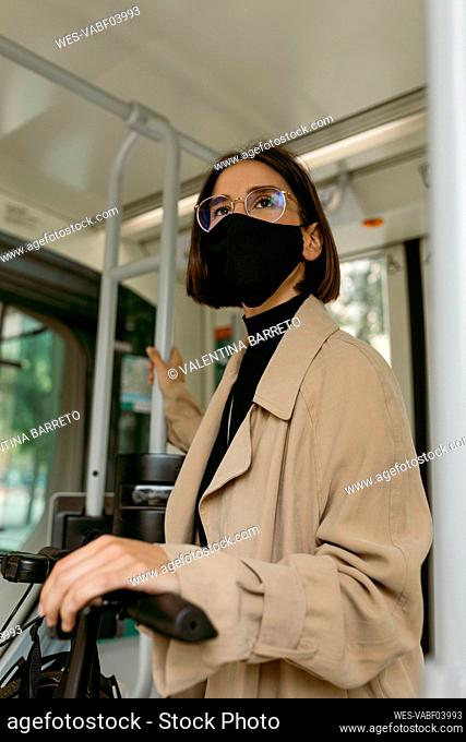 Mid adult woman wearing face mask standing with push scooter in tram