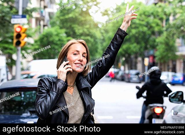 Woman with hand raised talking on mobile phone at street