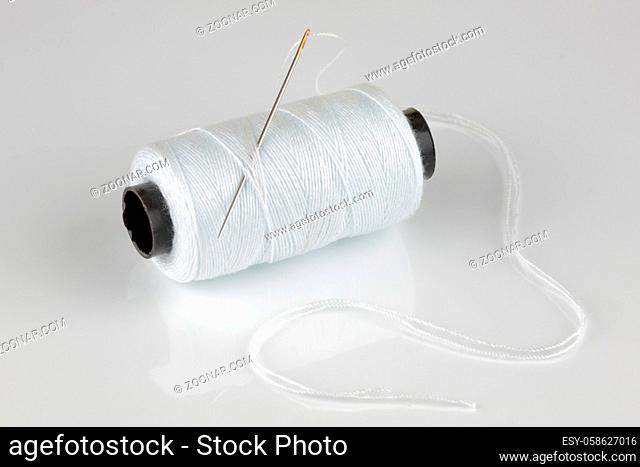 A white cotton reel and needle with reflection