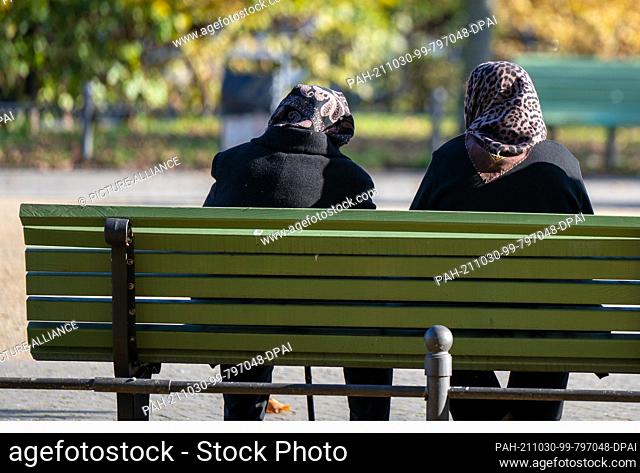 29 October 2021, Berlin: Two women with headscarves sit on a park bench Photo: Monika Skolimowska/dpa-Zentralbild/dpa. - Berlin/Berlin/Germany